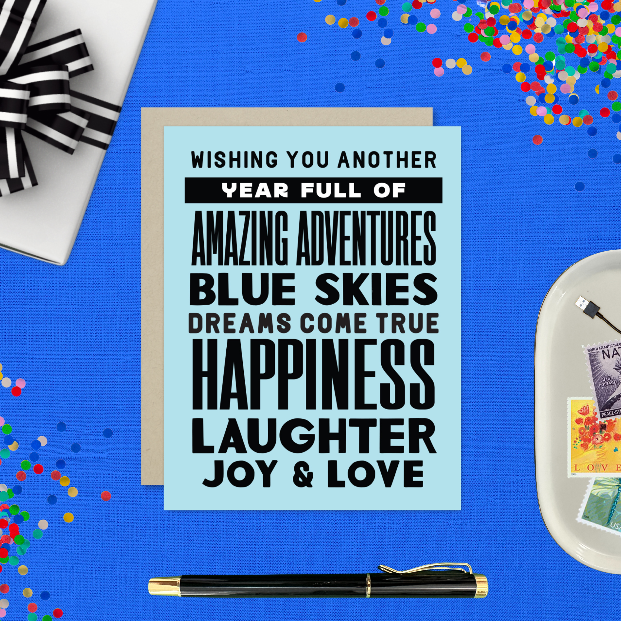 A birthday greeting card with blue background and black text, featuring stacked words and phrases like 'amazing adventures', 'blue skies', 'dreams come true', 'happiness', 'laughter', 'joy & love'