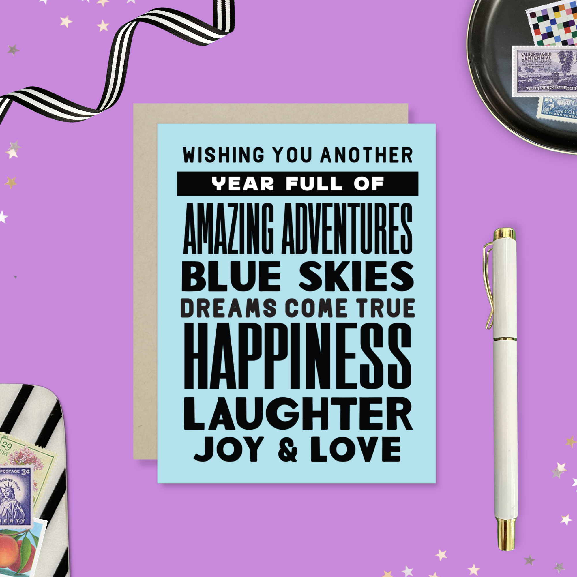 A birthday greeting card with blue background and black text, featuring stacked words and phrases like 'amazing adventures', 'blue skies', 'dreams come true', 'happiness', 'laughter', 'joy & love'