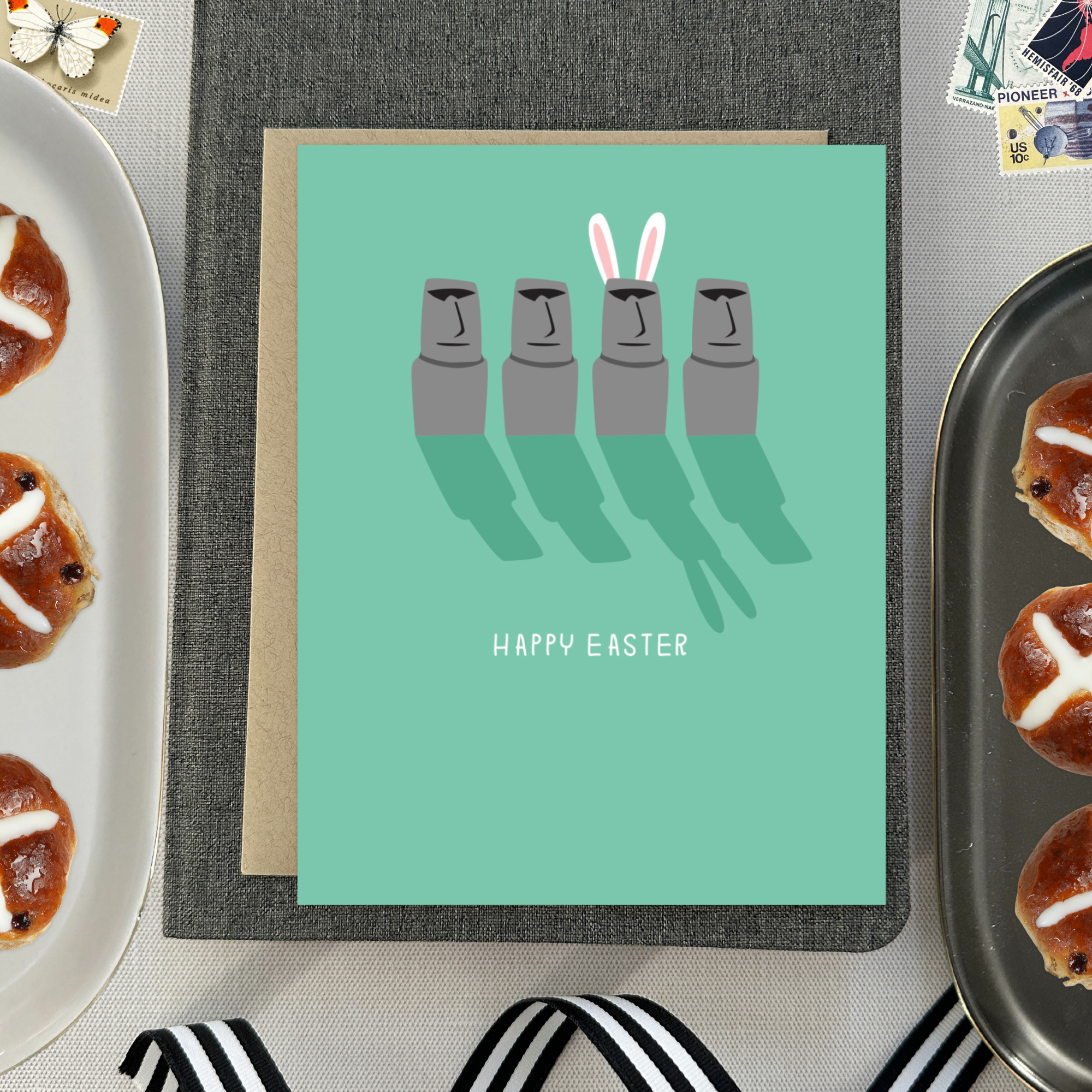 Easter greeting card with Easter island heads, one is wearing bunny ears with 'happy easter' text