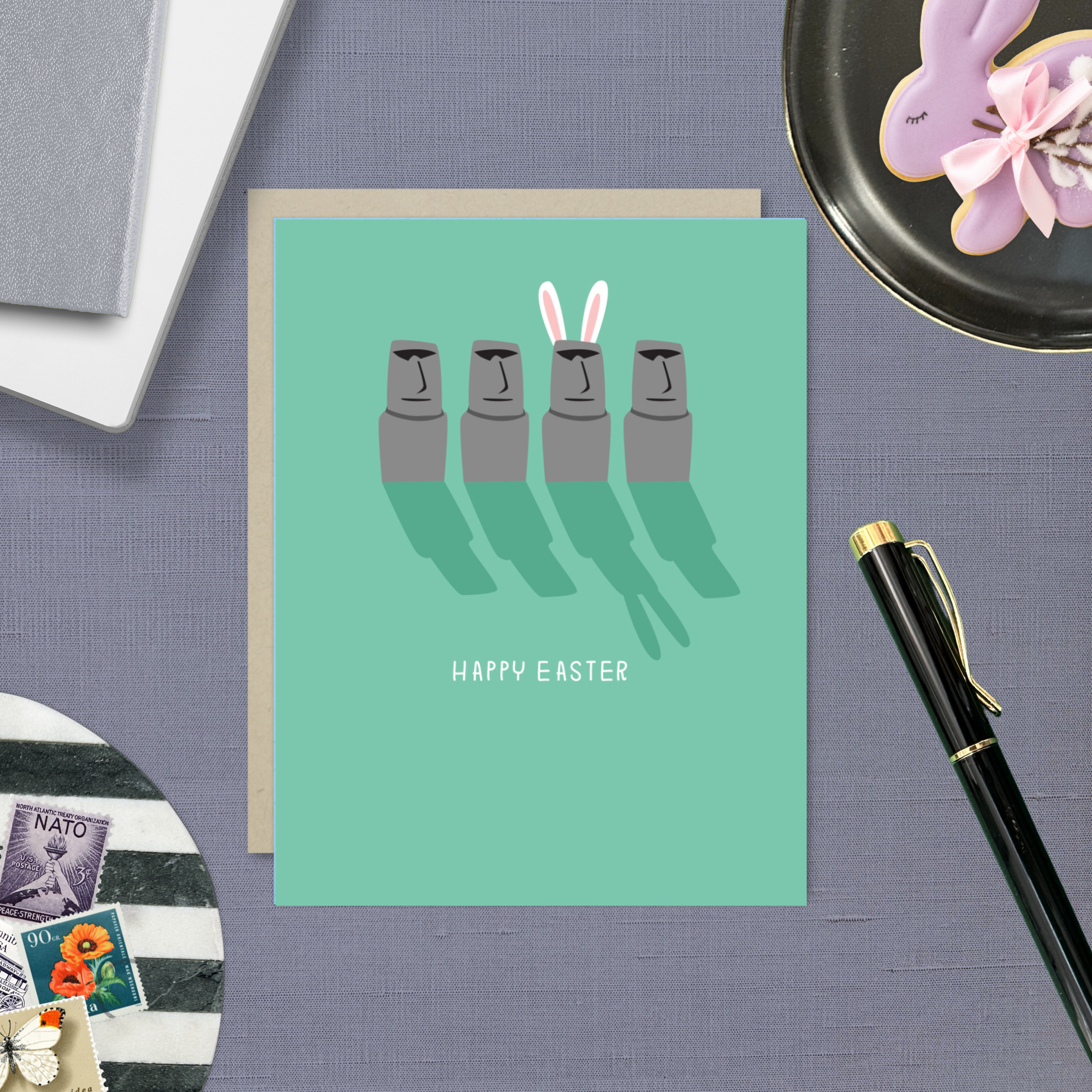 Easter greeting card with Easter island heads, one is wearing bunny ears with 'happy easter' text