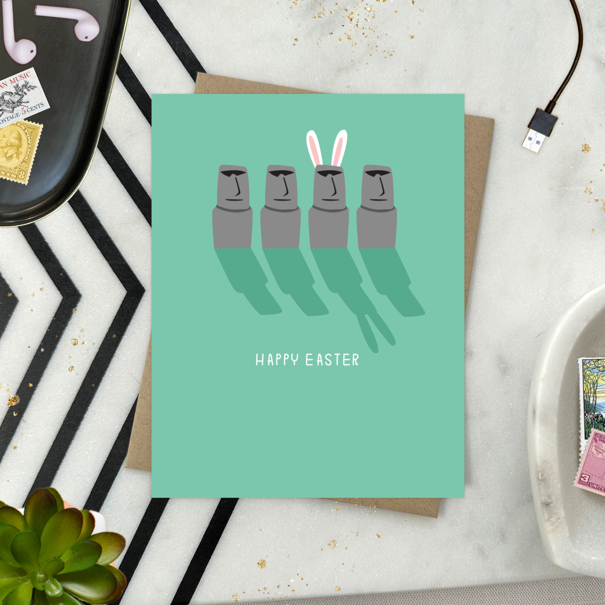 Easter greeting card with Easter island heads, one is wearing bunny ears with 'happy easter' text