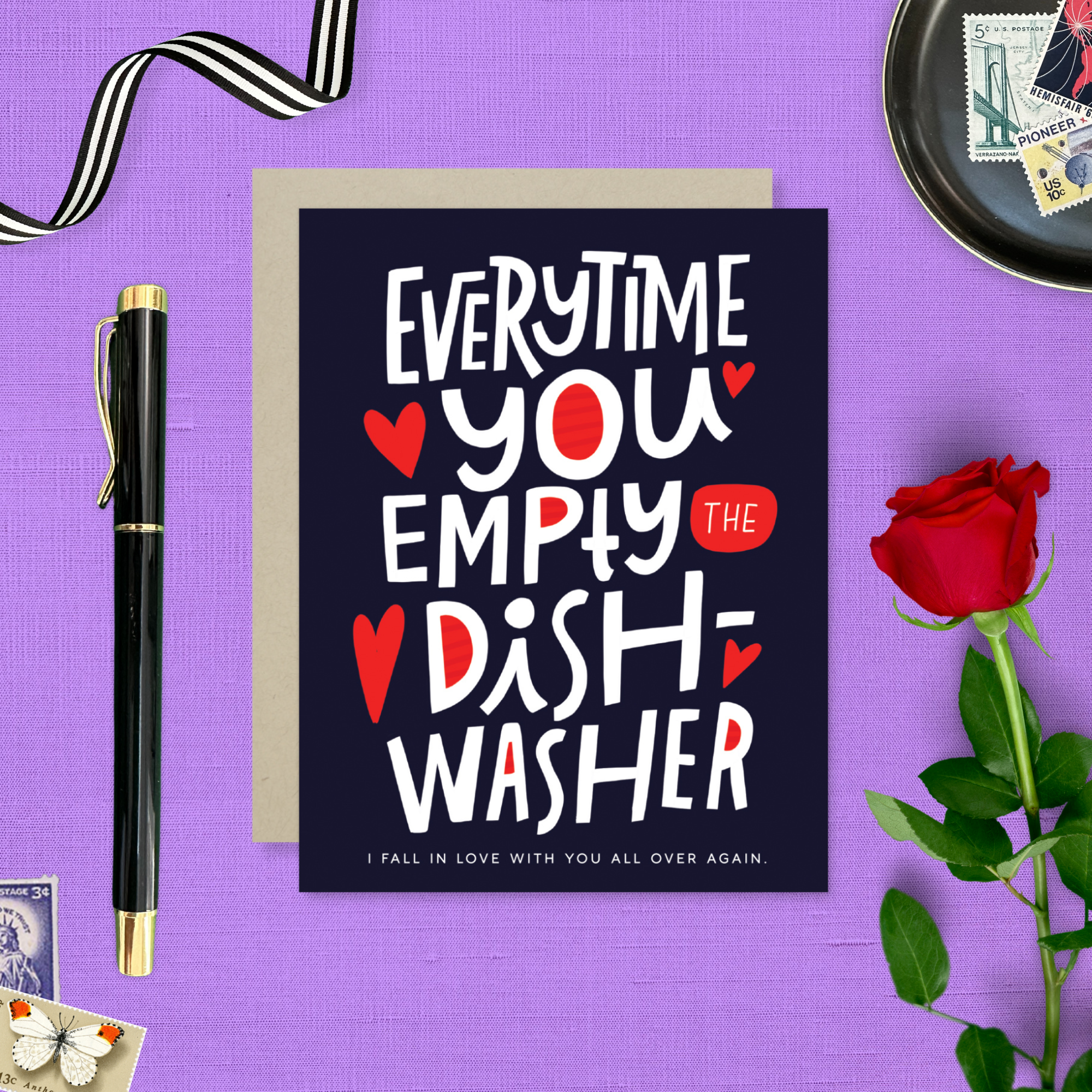 A Valentine's day greeting card with hand lettering that reads 'Everytime you empty the dishwasher I fall in love with you all over again.' It features red and red-hearts-shaped text on a dark background.