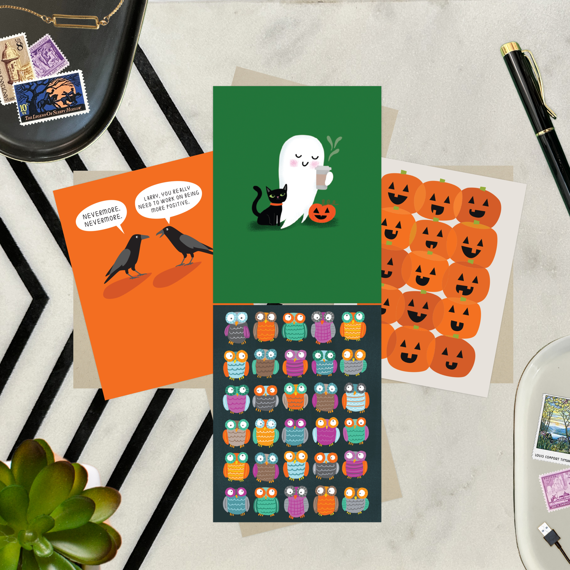Collection of Halloween-themed cards featuring an adorable ghost with black cat and coffee, one with 2 funny ravens saying "Nevermore," one with a jack-o-lantern pattern, and one with an owl pattern, on a table with a plant and pen.