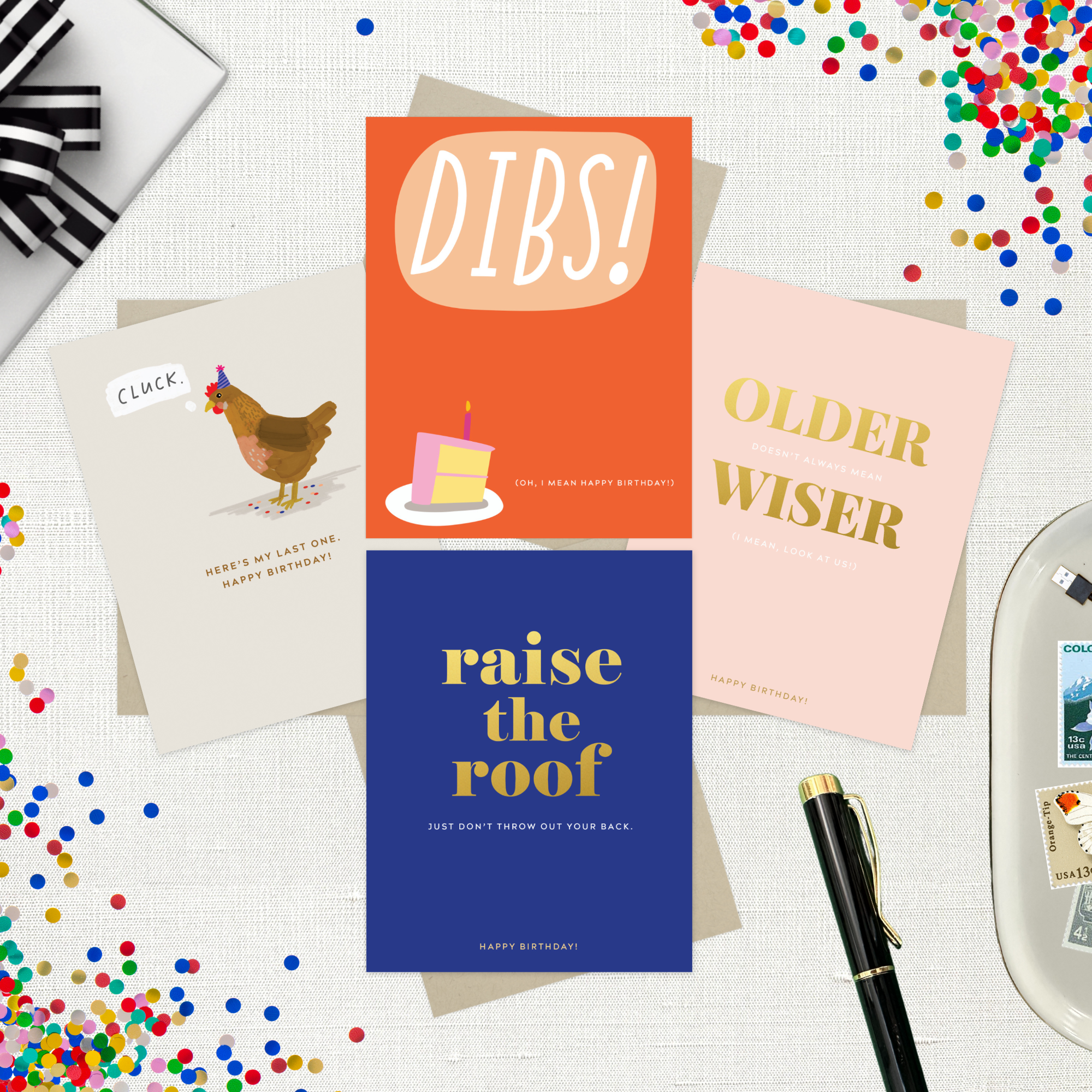 4-pack of funny birthday cards created by Barone & Co. featuring a chicken's last cluck, raise the roof but don't throw your back out, older but not wiser, and dibs on your birthday cake on white linen background with colorful confetti