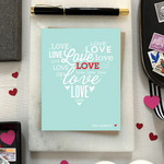 A heart-shaped Valentine's Day greeting card with the word 'love' arranged in a heart pattern using different fonts on a teal background, with a brown envelope.