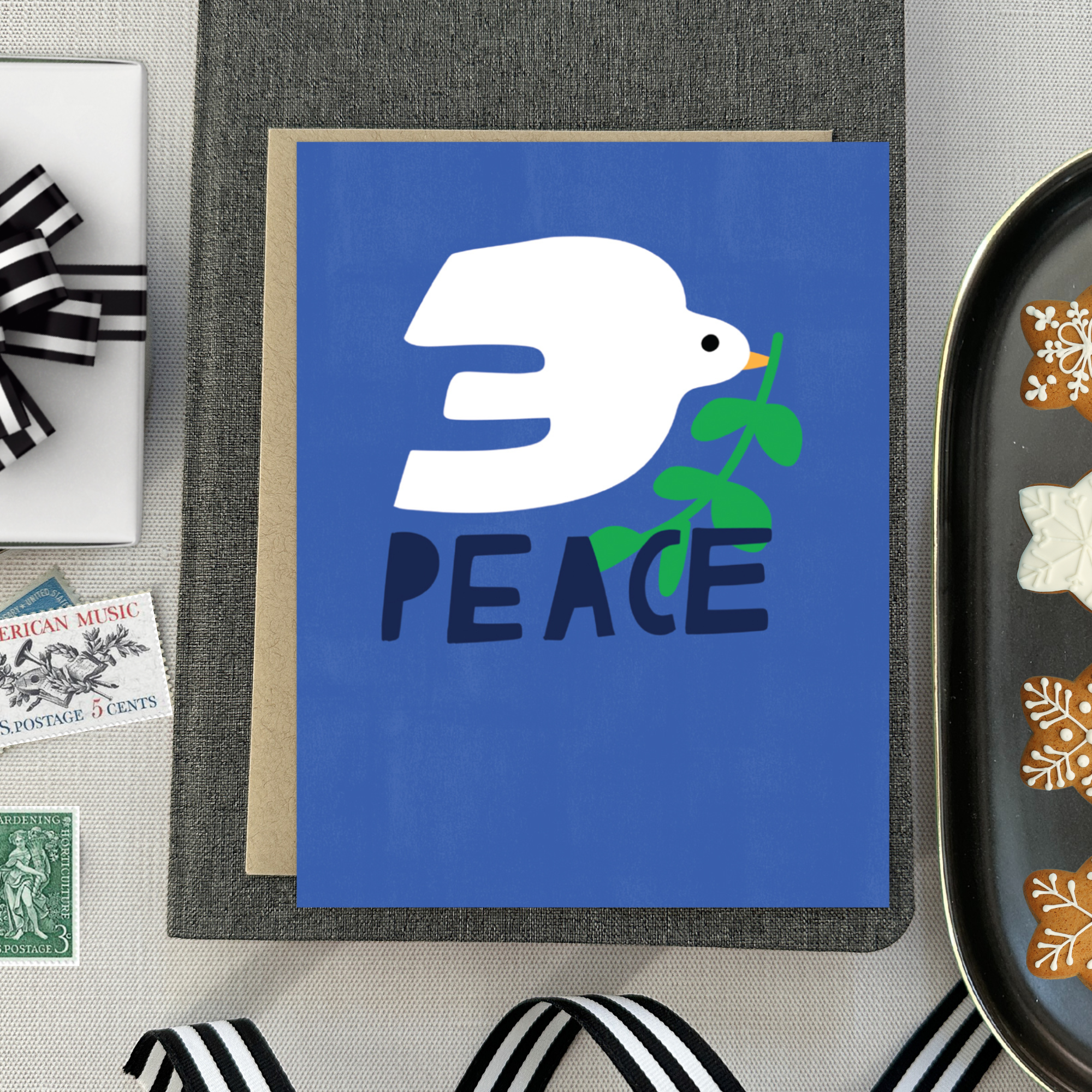 hand-painted holiday reeting card with a blue background featuring a white bird and the word 'PEACE' in capital letters.