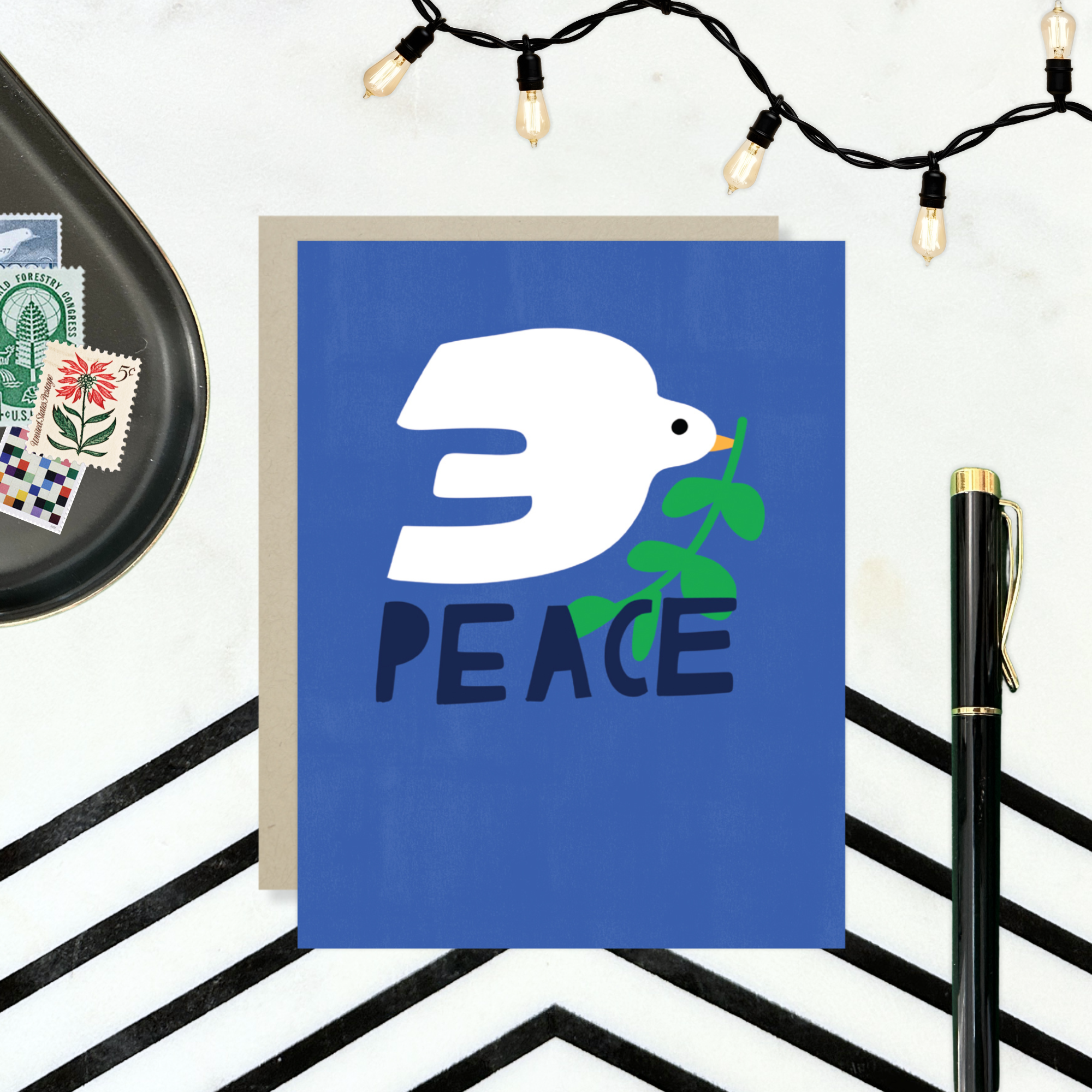 hand-painted holiday reeting card with a blue background featuring a white bird and the word 'PEACE' in capital letters.