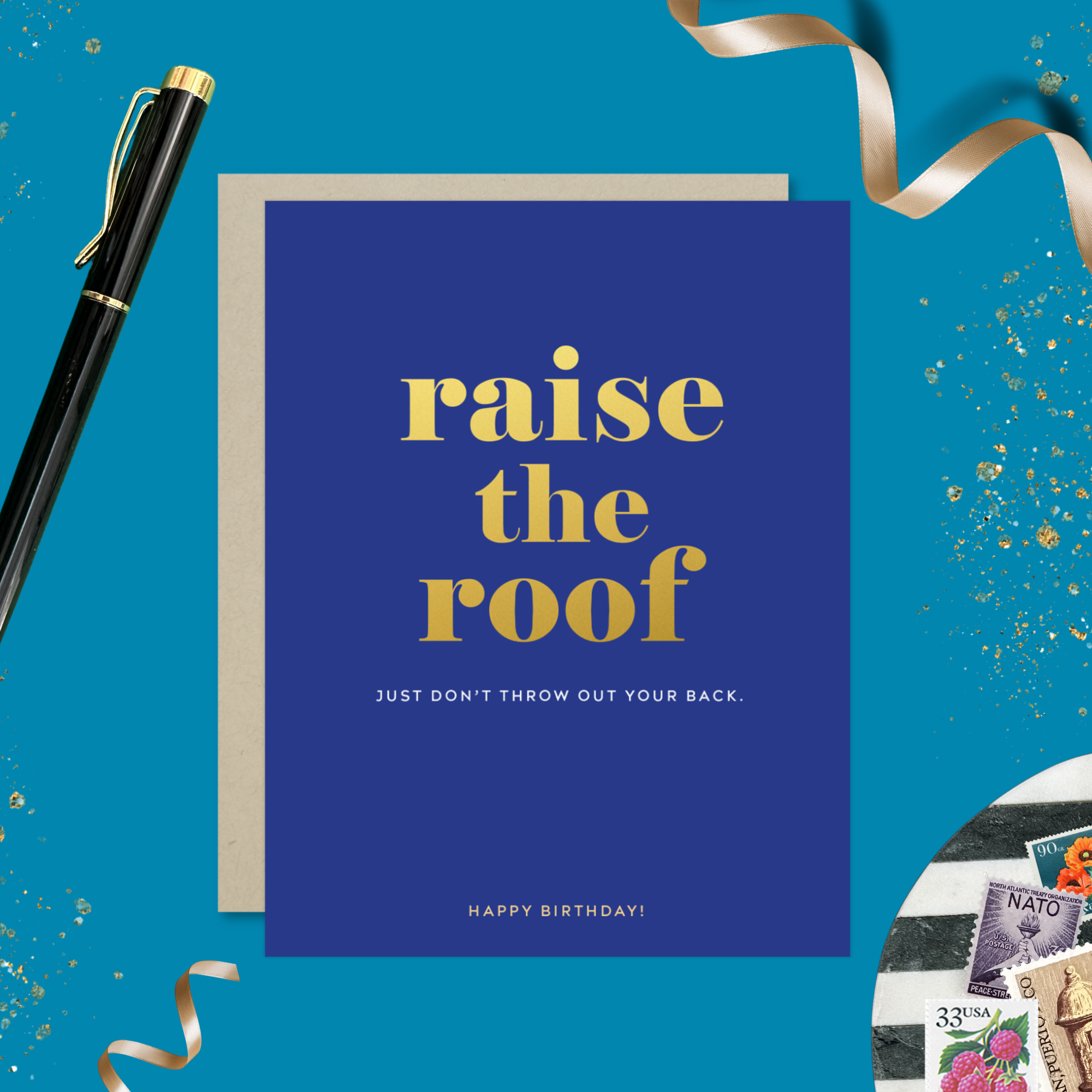 A birthday greeting card with 'raise the roof' printed in gold foil. Below it, in smaller gold foil text, reads 'Just don’t throw out your back.