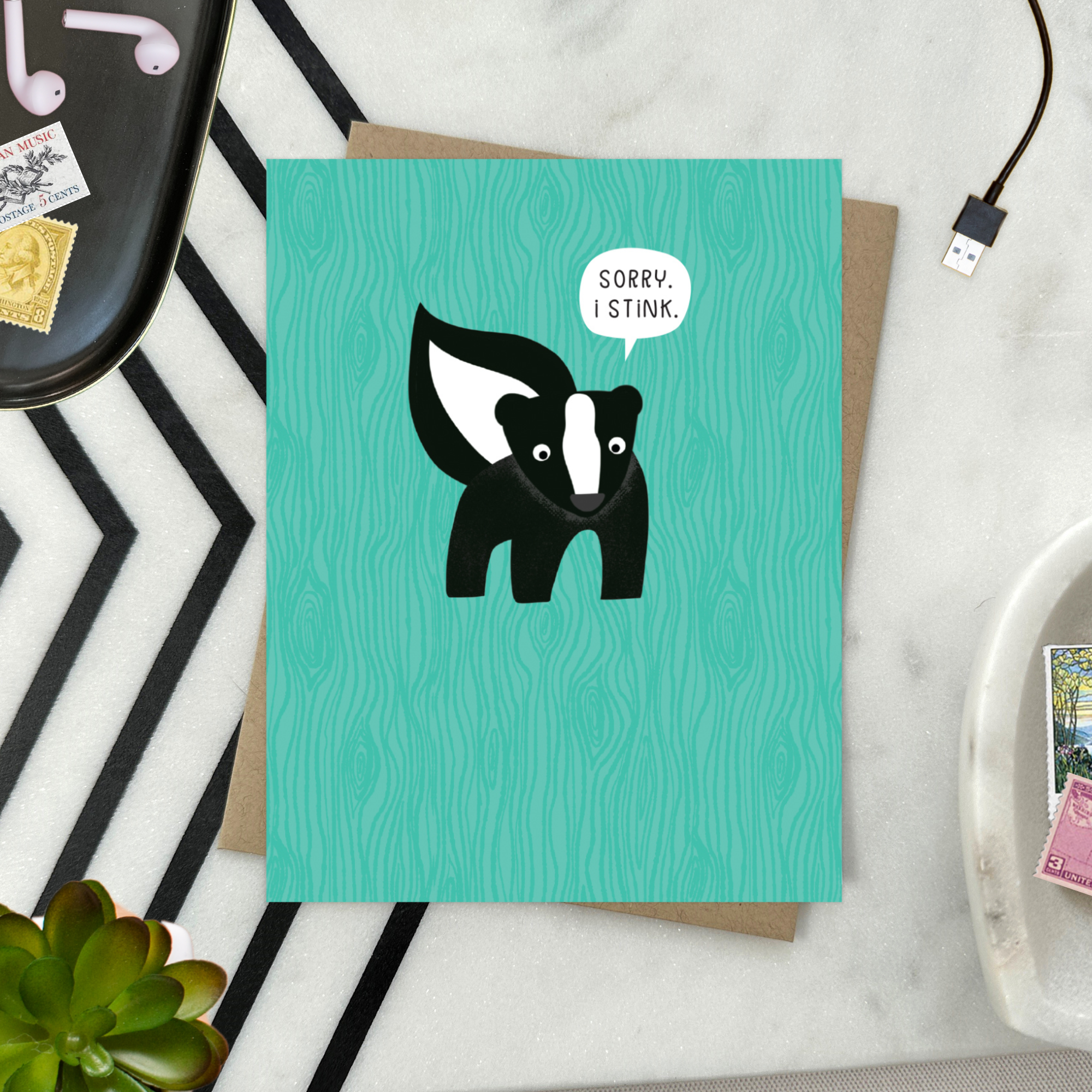 A sorry greeting card with an illustration of a skunk and the text 'Sorry I Stink' on a teal background.