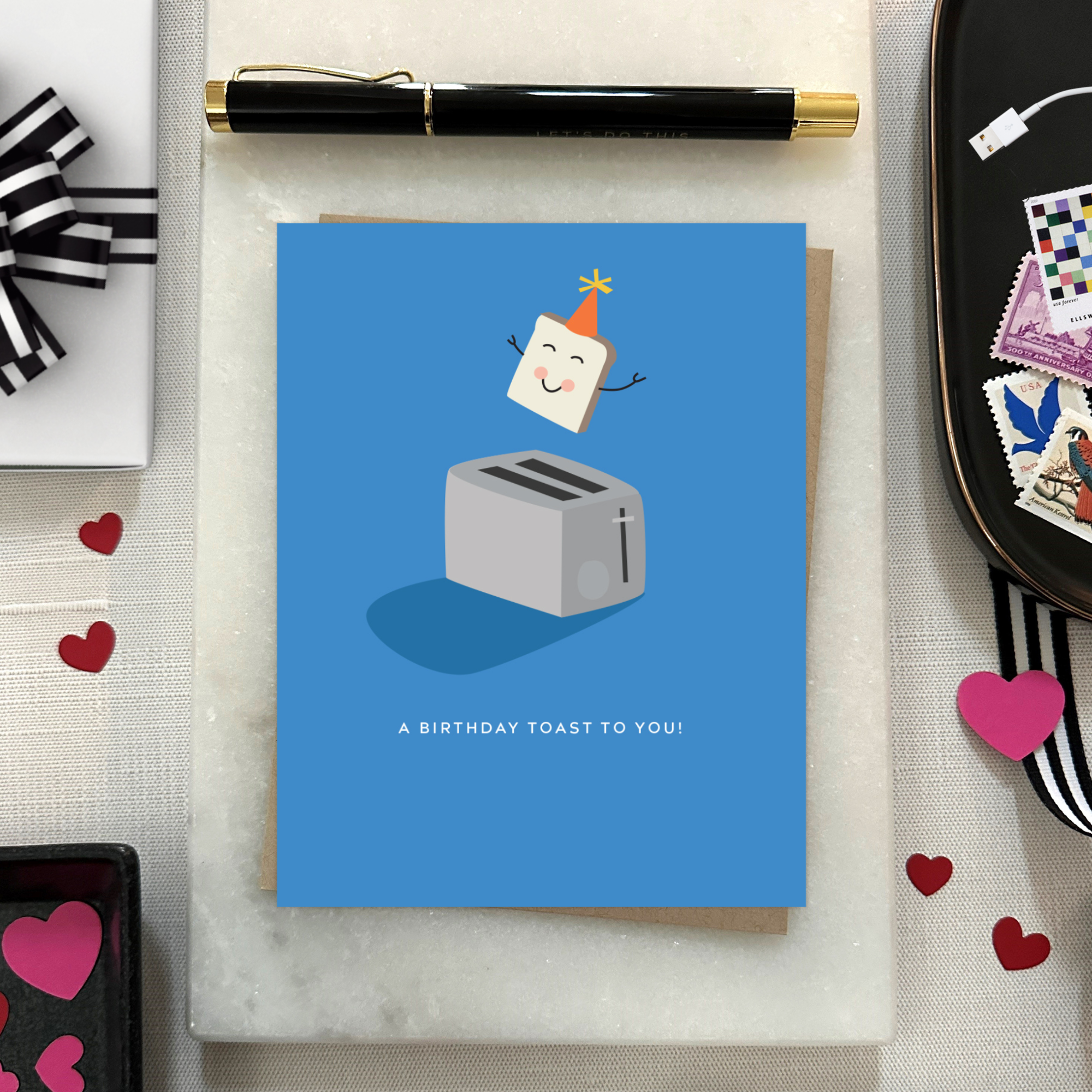 A playful birthday greeting card with an illustration of a smiling slice of toast with a party hat popping out of a toaster, and the text 'A Birthday Toast to You!'.