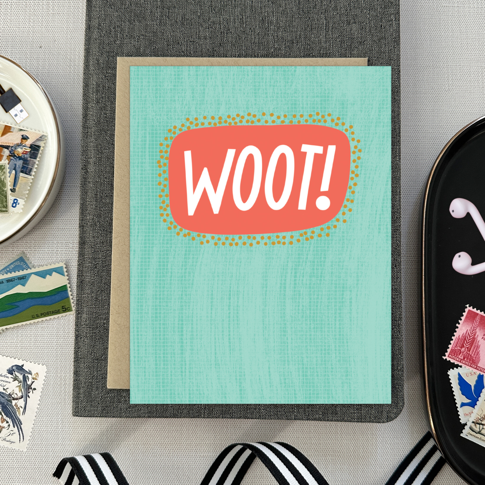 A congratulations greeting card with a hand-lettered word 'Woot!' written in bold, fun typography on a teal background with a textured appearance.