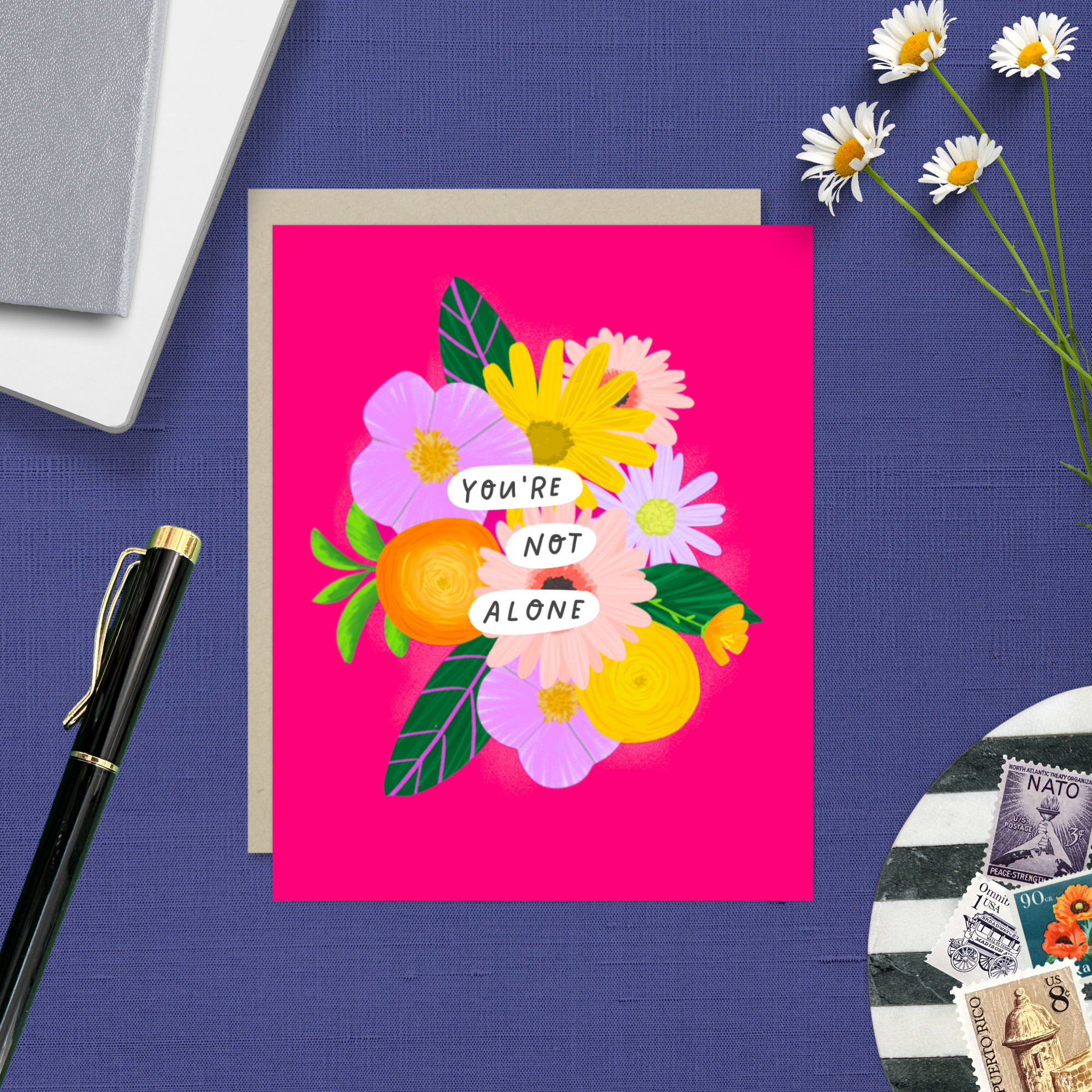 Colorful friendship or encouragement greeting card featuring a modern floral bouquet in pinks, oranges, yellows, and lavenders with the handwritten words, "You Are Not Alone" on a hot pink background with an included kraft envelope.