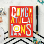 A colorful congratulations greeting card with the word 'CONGRATULATIONS' written in bold, playful lettering, predominantly in red, with additional decorative elements like stars.