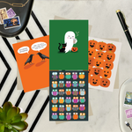 Collection of Halloween-themed cards featuring an adorable ghost with black cat and coffee, one with 2 funny ravens saying "Nevermore," one with a jack-o-lantern pattern, and one with an owl pattern,  on a table with a plant and pen.