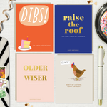 4-pack of funny birthday cards created by Barone & Co. featuring a chicken's last cluck, raise the roof but don't throw your back out, older but not wiser, and dibs on your birthday cake on white linen background with ribbons and confetti