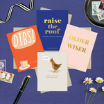4-pack of funny birthday cards created by Barone & Co. featuring a chicken's last cluck, raise the roof but don't throw your back out, older but not wiser, and dibs on your birthday cake on a dark purple background with stamps and flowers
