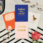4-pack of funny birthday cards created by Barone & Co. featuring a chicken's last cluck, raise the roof but don't throw your back out, older but not wiser, and dibs on your birthday cake surrounded by gold confetti and ribbons on black and white background