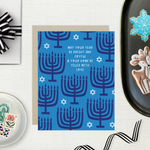Hannukah greeting card with menorahs and stars of David scattered with 'may your year be bright and joyful & your home be filled with love' text