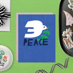  hand-painted holiday reeting card with a blue background featuring a white bird and the word 'PEACE' in capital letters.