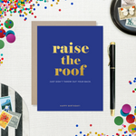 A birthday greeting card with 'raise the roof' printed in gold foil. Below it, in smaller gold foil text, reads 'Just don’t throw out your back.