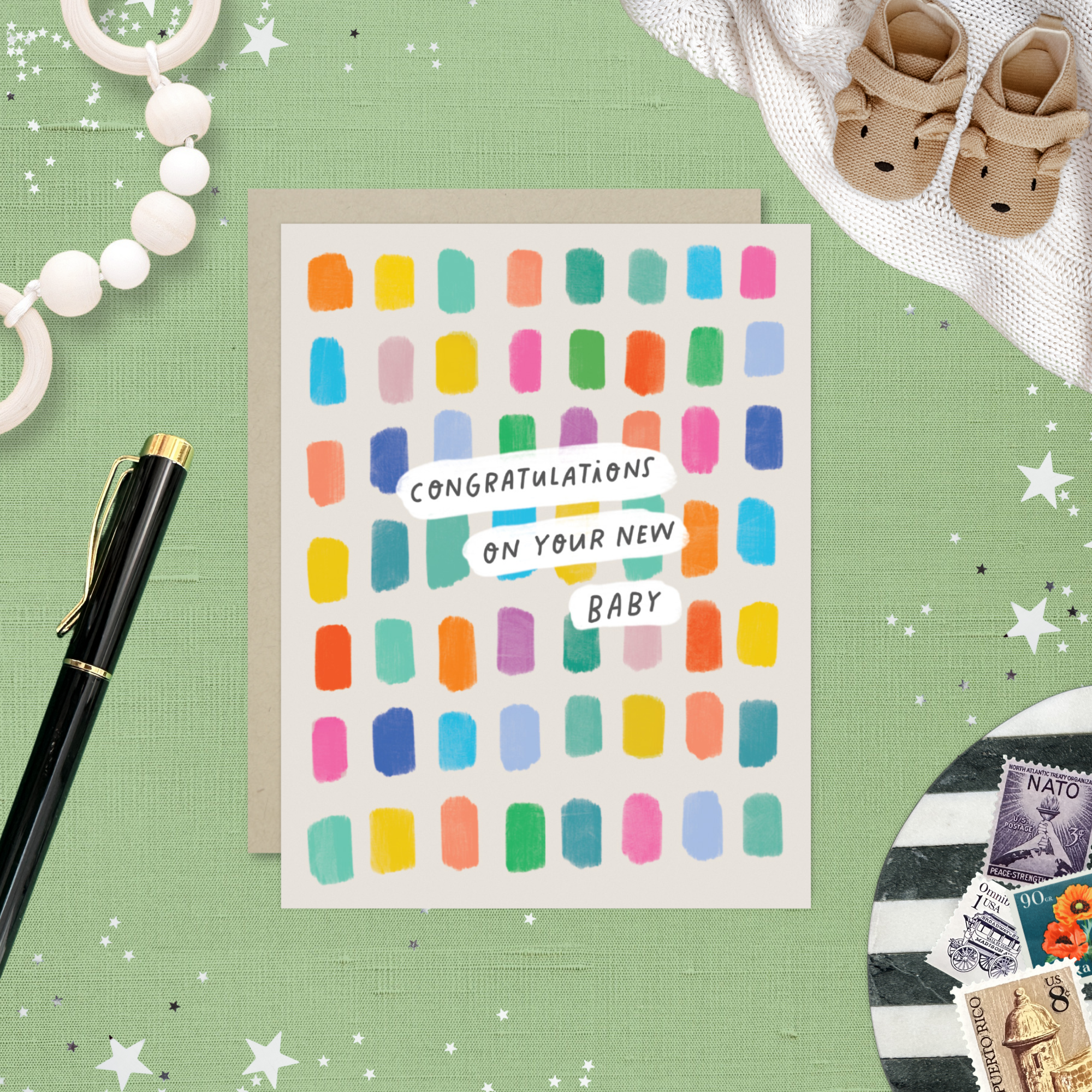 New baby colorful greeting card with 'Congratulations on your new baby' text on a green surface with baby items.