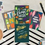 Four colorful greeting cards with Thanksgiving-themed designs on a striped surface featuring "I'm so grateful for you," "Happy Thanksgiving," "Feast Mode," and "So Thankful." 