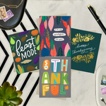 Four colorful greeting cards with autumn-themed designs on a marble surface featuring "I'm so grateful for you," "Happy Thanksgiving," "Feast Mode," and "So Thankful."