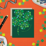 A st. patricks day greeting card with a pattern of tiny illustrated shamrocks arranged in the shape of a larger four-leaf clover, and the text 'Happy St. Patrick's Day' 