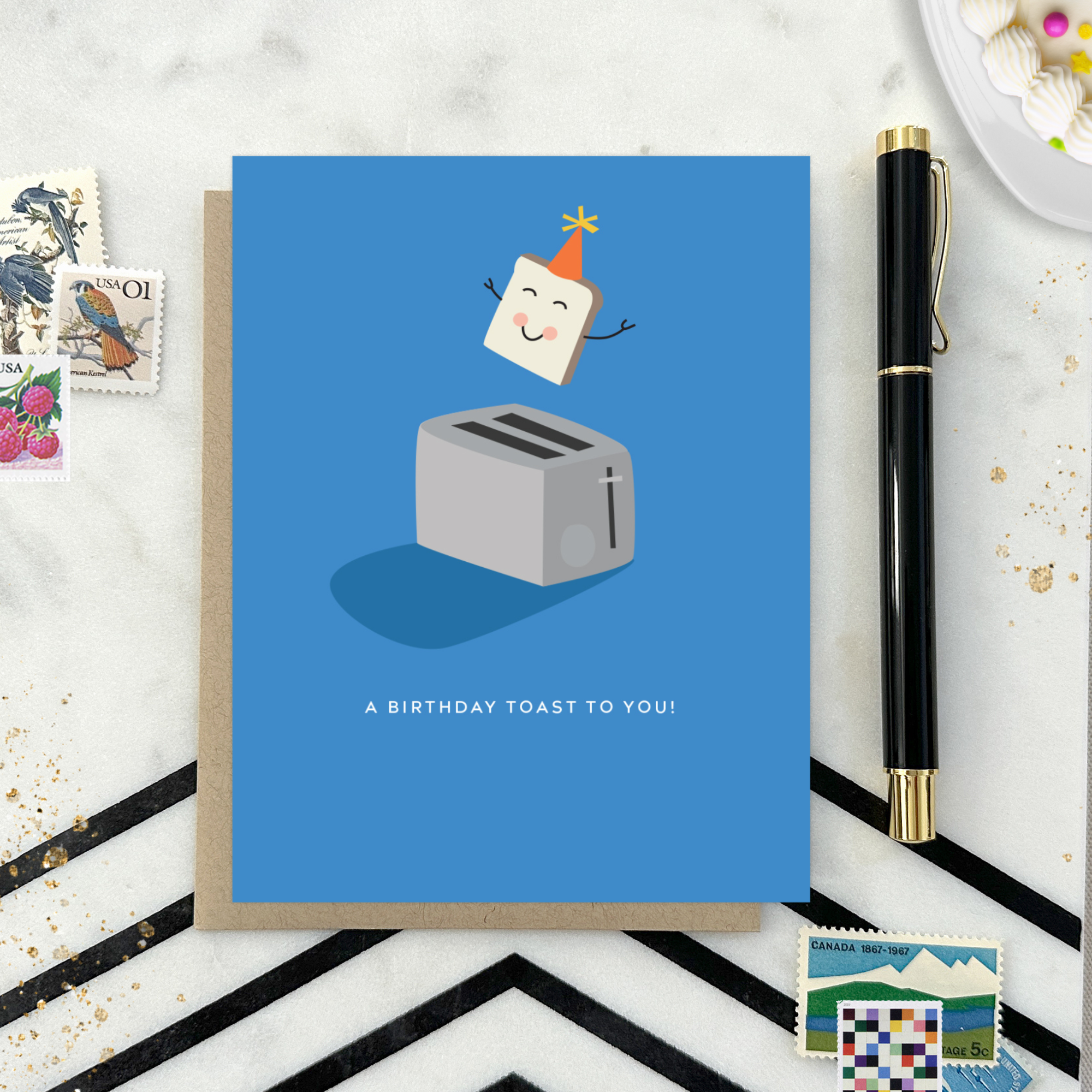 A playful birthday greeting card with an illustration of a smiling slice of toast with a party hat popping out of a toaster, and the text 'A Birthday Toast to You!'.