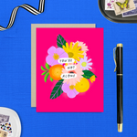 Colorful friendship or encouragement greeting card featuring a modern floral bouquet in pinks, oranges, yellows, and lavenders with the handwritten words, "You Are Not Alone" on a hot pink background with a matching kraft envelope.